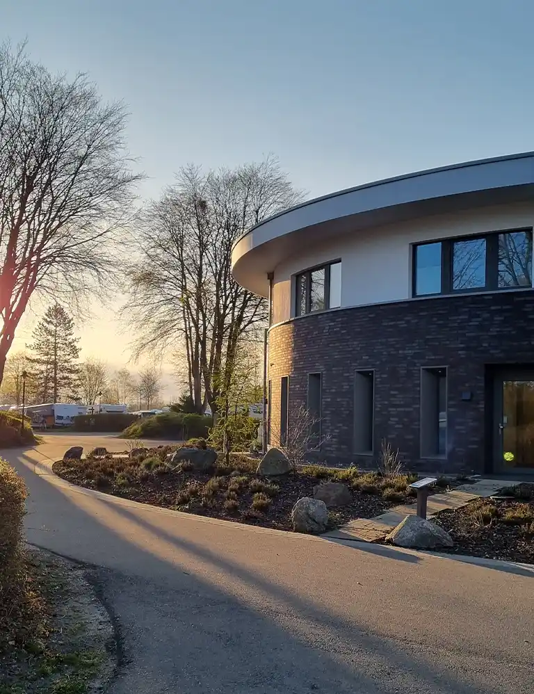 Besondere Ausstattung ansehen Modernes rundes Sanitärgebäude im Südsee-Camp im Abendlicht mit umliegenden Bäumen und Stellplätzen