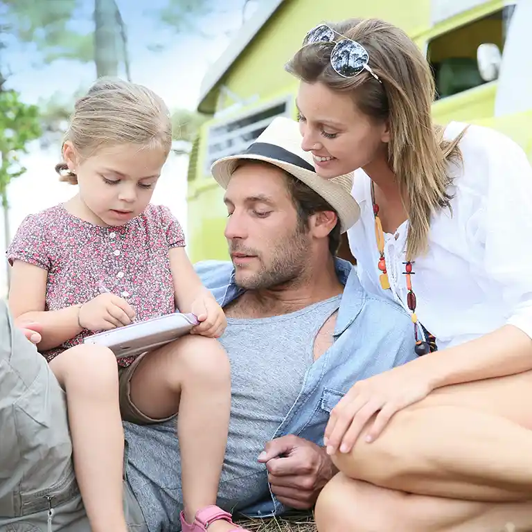Familie mit kleinem Mädchen beim gemeinsamen Zeichnen vor einem Wohnmobil – entspanntes Camping mit Kindern in der Natur