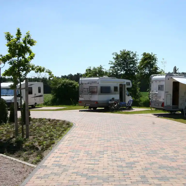 Wohnmobilstellplatz vor dem Südsee-Camp mit gepflastertem Weg, parkenden Wohnmobilen und Sitzgelegenheiten im Grünen