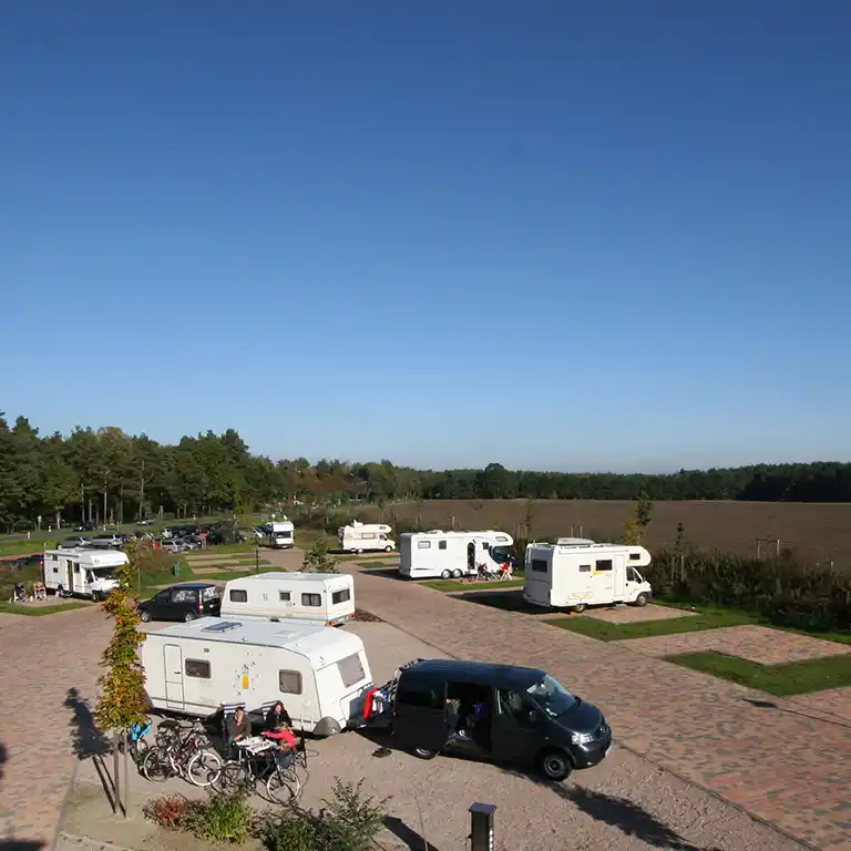 Übernachtungsoase vor dem Südsee-Camp mit Wohnmobilen und Wohnwagen auf gepflasterten Stellflächen, umgeben von Feldern und Wald