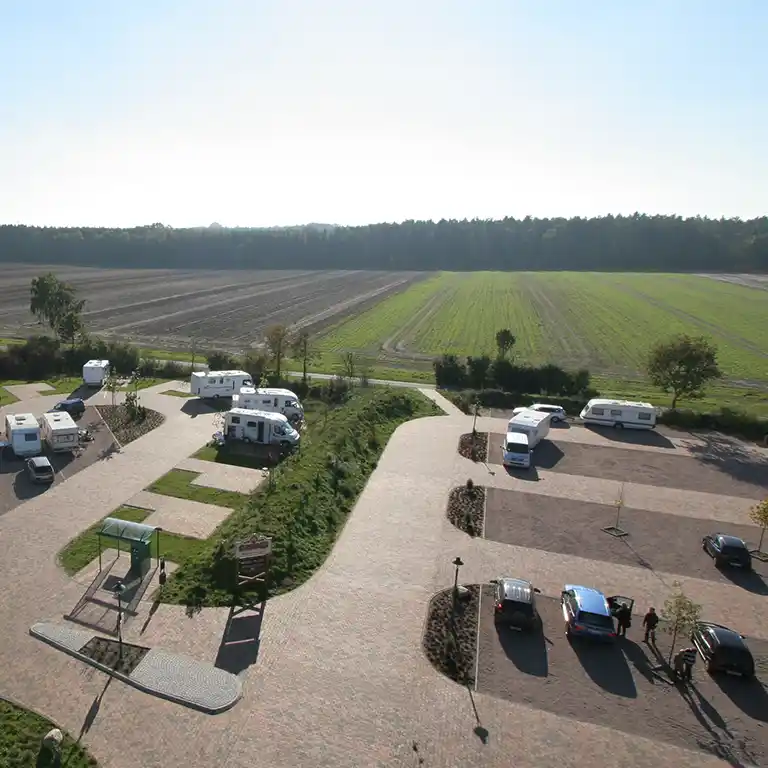Luftaufnahme des Wohnmobilstellplatzes bei der Übernachtungsoase mit Wohnmobilen und gepflasterten Stellflächen, angrenzend an Felder und Waldrand