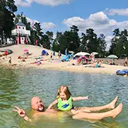 Sommerferien fröhlich posierender Papa mit Tochter im Badesee, Südsee-Camp Strand, Leuchtturm und weitere Familien im Hintergrund