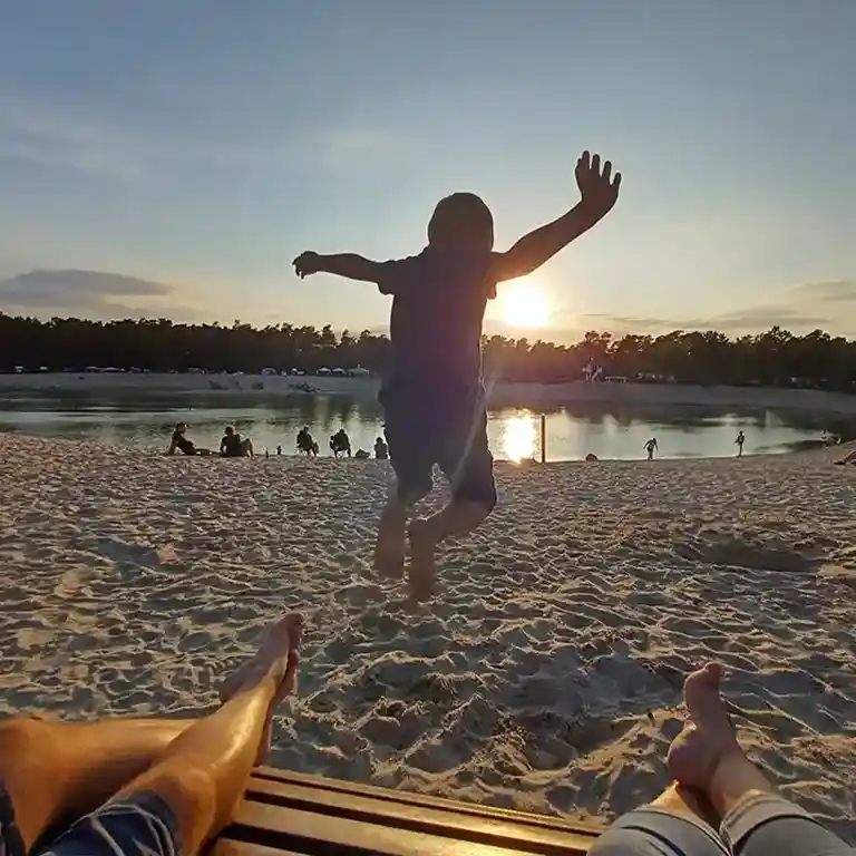 Hüpfendes Kind am Strand, im Hintergrund der Badesee