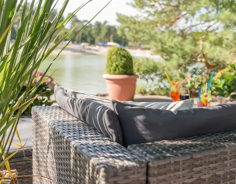 mehrere Restaurants & Bistros auf dem Campingplatz Gemütliche Lounge-Sitzecke mit Blick auf den See beim Insel-Restaurant im Südsee-Camp, auf dem Tisch bunte Sommergetränke mit Strohalmen.