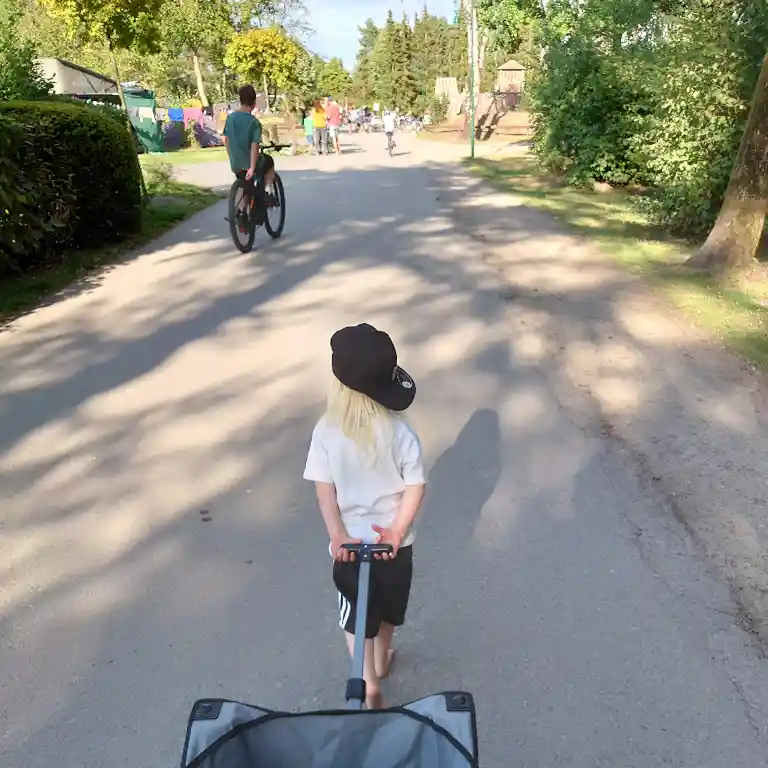Kind zieht einen Bollerwagen und im Hintergrund ein Kind auf einem Fahrrad