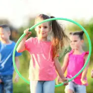 Hulahoop Mädchen mit Hulahoop-Reifen in der Hand, Kinder im Hintergrund