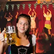 Oktoberfest Frau im Dirndl mit Bierkrug, tanzende Personen im Hintergrund