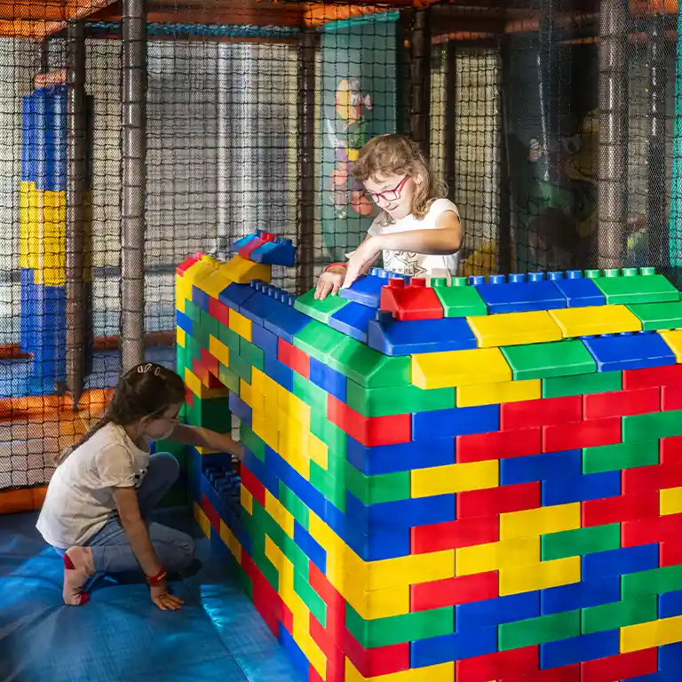 Zwei Mädchen bauen mit großen bunten Bausteinen im Indoorspielplatz „Piratennest“ im Südsee-Camp. Kreatives Spielen und gemeinsames Bauen machen den Familienurlaub zu einem besonderen Erlebnis.