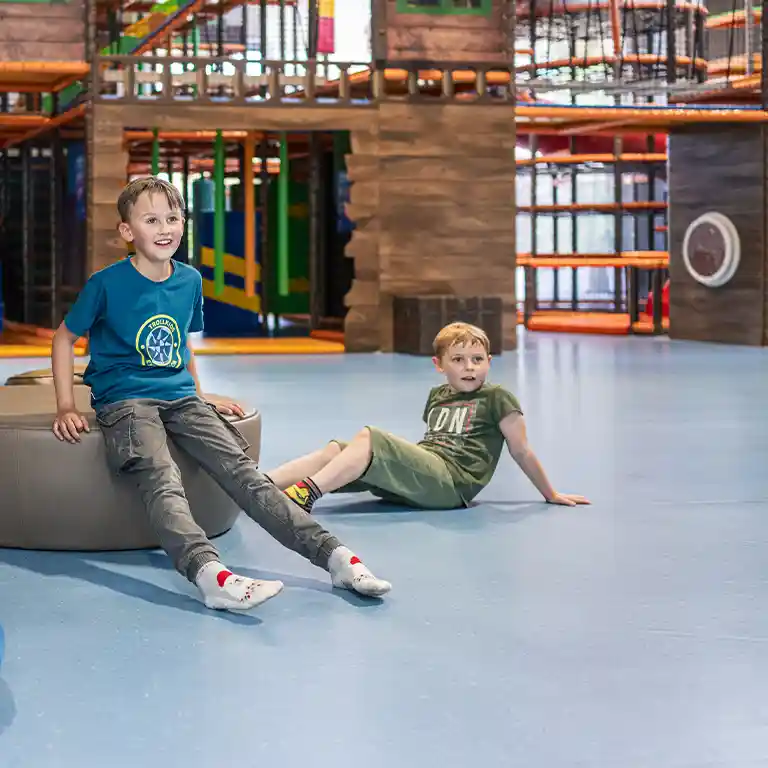 Zwei Jungen spielen im Indoorspielplatz „Piratennest“ im Südsee-Camp. Sie sitzen lachend auf dem Boden vor der großen Kletter- und Abenteuerlandschaft – ein Ort voller Spielspaß für Kinder im Familienurlaub.