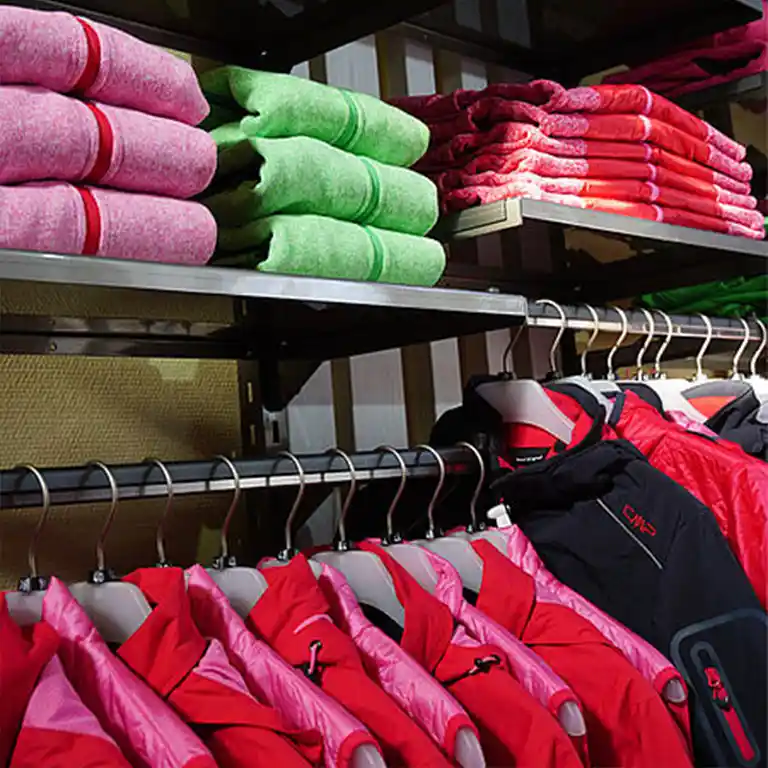 Rote Outdoorjacken auf Kleiderbügeln und gefaltete Vliesjacken in Pink, Grün und Rot im Regal des Südsee-Trends Shops.