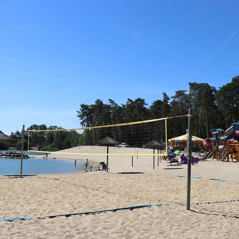 Mehr erfahren Feiner Sandstrand mit Beachvolleyballfeld, flachem Zugang zum See und einem Spielplatz mit gut erreichbaren Wegen – ein entspannter Ort für Familien.