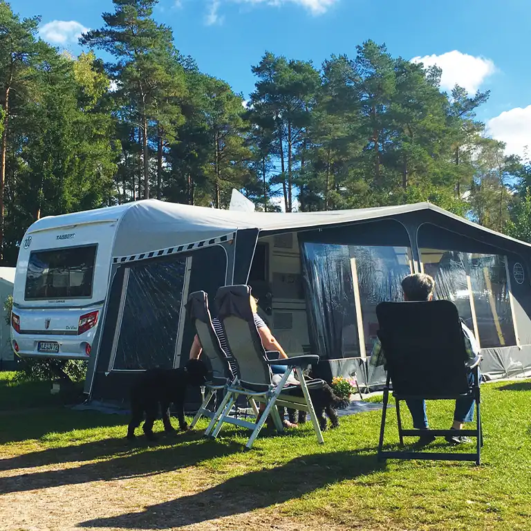 Campingplatz erkunden Wohnwagen mit Vorzelt und Campingstühlen auf sonnigem Stellplatz im Grünen