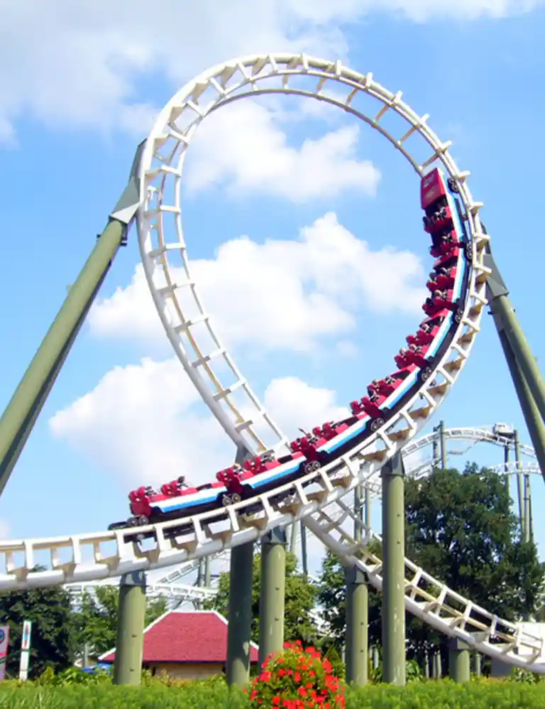 to the amusement park Roller coaster with a loop at Heide Park under a blue sky – thrilling amusement park fun for the whole family in Northern Germany’s largest theme park.