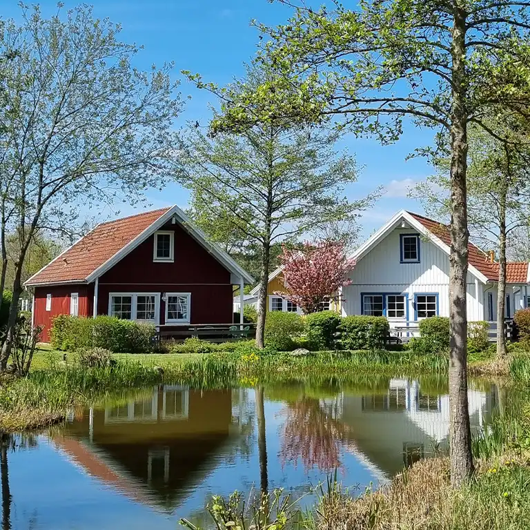 Urlaub in Sommarbÿ Zwei Holzferienhäuser mit rotem und weißem Anstrich am Biotop mit Spiegelung im Wasser
